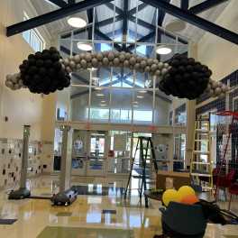 Black and gray balloon arch in a lobby with ladders and chairs