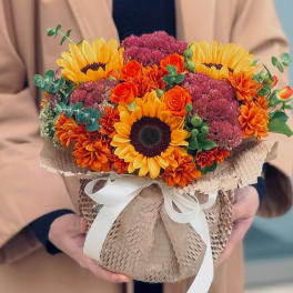 Bouquet of sunflowers, orange roses, and burgundy blooms wrapped in kraft paper