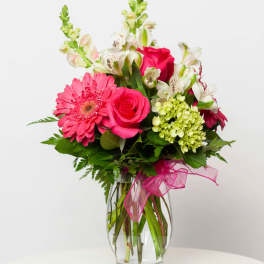 Pink gerbera daisies and roses in a clear glass vase with a pink ribbon