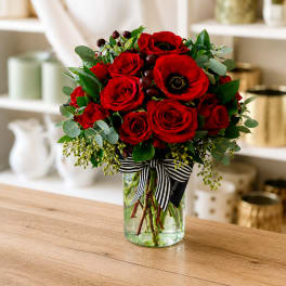 Red roses and anemones in a glass vase with a striped ribbon