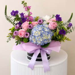 Pink and purple mixed bouquet in a black hat box with a lavender ribbon