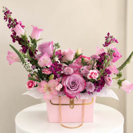 Pink and purple mixed flower arrangement in a pink handbag-style box