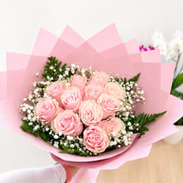 Handheld bouquet of pink roses wrapped in pink paper