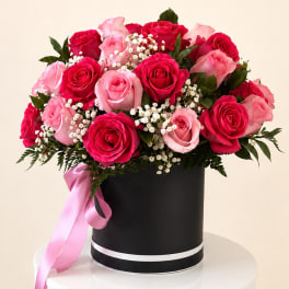 Pink and red roses arranged in a black hatbox with a pink ribbon