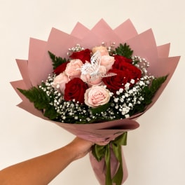 Handheld bouquet of red and blush roses with baby's breath in pink wrap