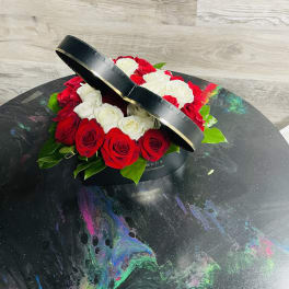 Red and white roses arranged in a black round box with a lid propped open