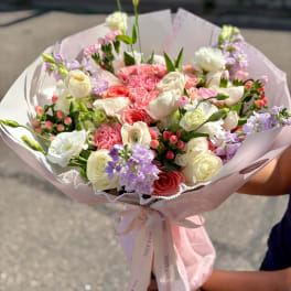 Hand-tied bouquet of pink, white, and lavender flowers wrapped in pale pink paper