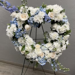 Heart-shaped floral wreath with white and blue flowers on a stand