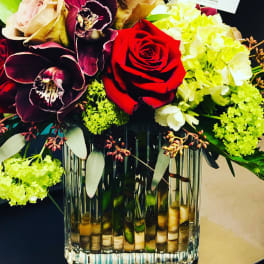 Bouquet of red roses, orchids, and pale hydrangeas in a glass vase