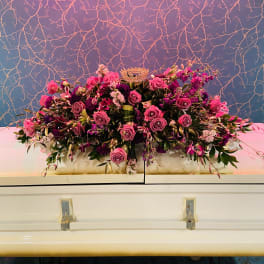 Large pink and purple floral casket spray with a crown topper