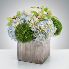 Arrangement of white and pale blue flowers in a square wooden vase