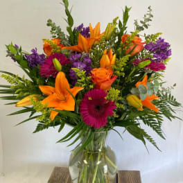 Bouquet of orange lilies, roses, and purple flowers in a glass vase