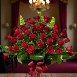 Red roses arranged in a clear vase with a burgundy ribbon