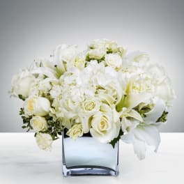 Compact arrangement of white roses, hydrangeas, and lilies in a square glass vase
