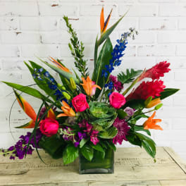 Tropical bouquet with roses, lilies, and blue delphinium in a glass vase