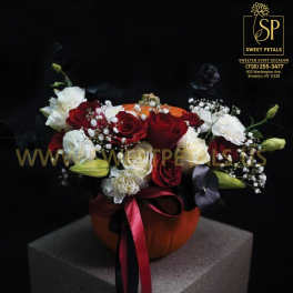 Red and white rose arrangement in an orange pumpkin vase with ribbon