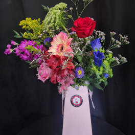 Mixed bouquet in a pink gift box with red, pink, purple, and blue flowers