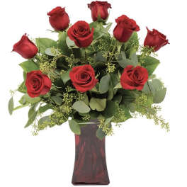 Red roses arranged in a tall glass vase with greenery
