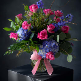 Pink roses and blue hydrangeas in a glass vase with a pink ribbon