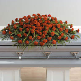 Orange carnation casket spray with palm fronds on a light gray casket
