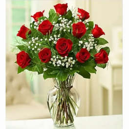 Red roses arranged in a clear glass vase with small white filler flowers