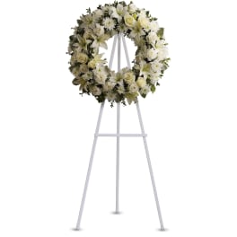 White floral wreath with roses, lilies, and mums on a tall white easel stand