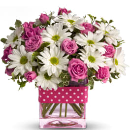 Short arrangement of white daisies and pink roses in a pink glass cube vase with a pink polka dot ribbon.