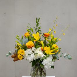 Yellow lilies and roses in a glass vase with white hydrangeas