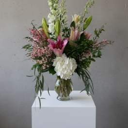 Tall bouquet of pink and white lilies in a clear glass vase