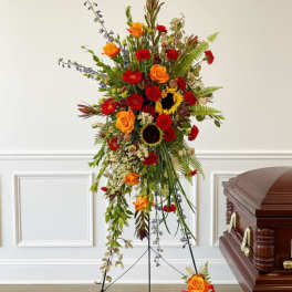 Tall funeral spray with red, orange, and yellow flowers beside a casket