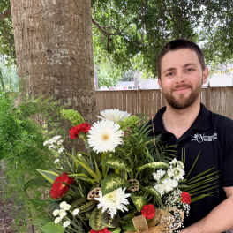 Large mixed flower arrangement in a dark bowl vase with a gold ribbon
