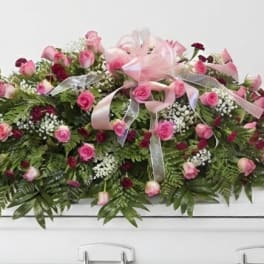 Pink rose casket spray with ribbon on a white casket