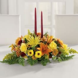 Low floral centerpiece with yellow and orange blooms and two red taper candles