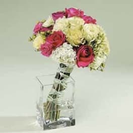 Hand-tied bouquet of hot pink and cream roses with white hydrangeas in a clear glass cube vase