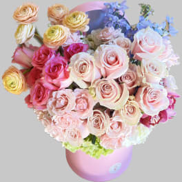 Bouquet of pink and peach roses with blue flowers in a pink hatbox