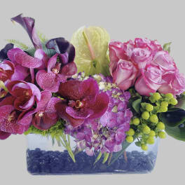 Pink roses and purple orchids in a clear rectangular vase