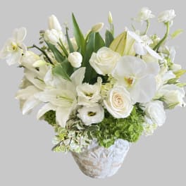 White floral arrangement in a textured vase with lilies, roses, and orchids
