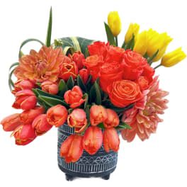 Bouquet of red and yellow tulips with orange roses in a patterned vase