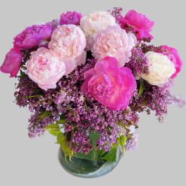 Pink peonies and lilac flowers arranged in a glass vase