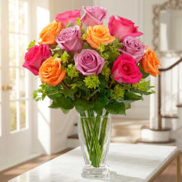 Bouquet of pink, purple, and orange roses in a clear glass vase