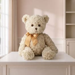 Cream teddy bear with a gold ribbon sitting on a table