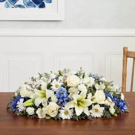 Low floral centerpiece with white lilies, roses, daisies, and blue accents