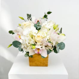 White floral arrangement in a square wooden vase with eucalyptus accents