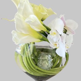 White calla lilies and orchids arranged in a glass bowl vase