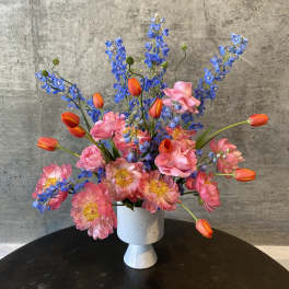 Pink and blue floral arrangement in a white pedestal vase