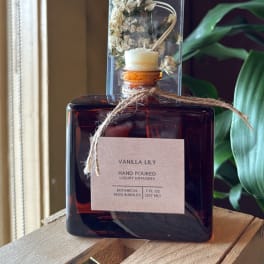 Amber reed diffuser bottle labeled Vanilla Lily with dried flowers