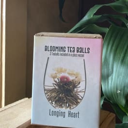 Box of blooming tea balls labeled Longing Heart beside green leaves