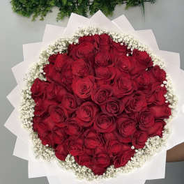 Round bouquet of red roses edged with white baby's breath and white wrap