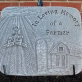 Gray memorial plaque with a farm scene and the words 'In Loving Memory of a Farmer'