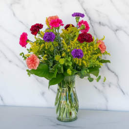 Mixed bouquet of carnations and yellow filler flowers in a clear glass vase